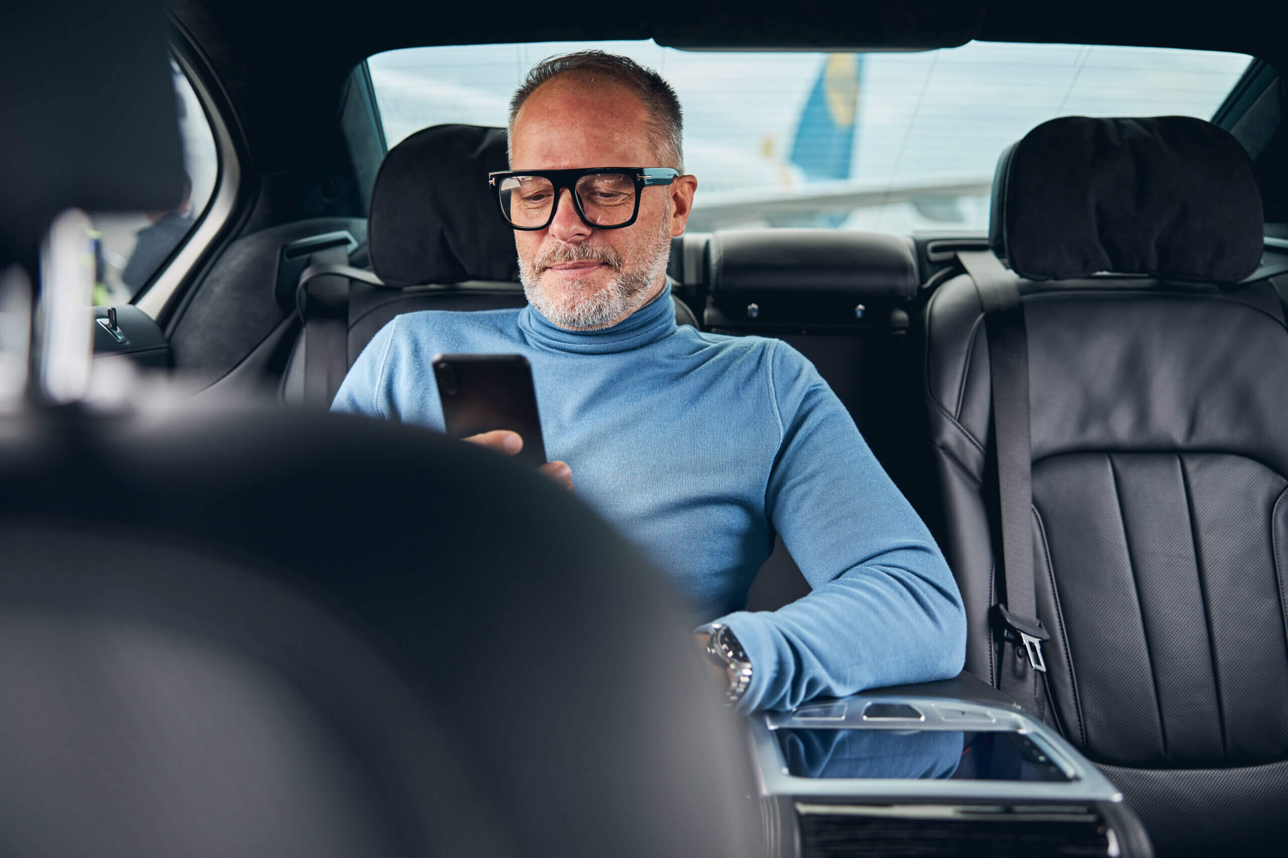 Ein Mann entspannt im Auto, während er auf sein Smartphone schaut. Ideal für Limousinenservice in Stuttgart.